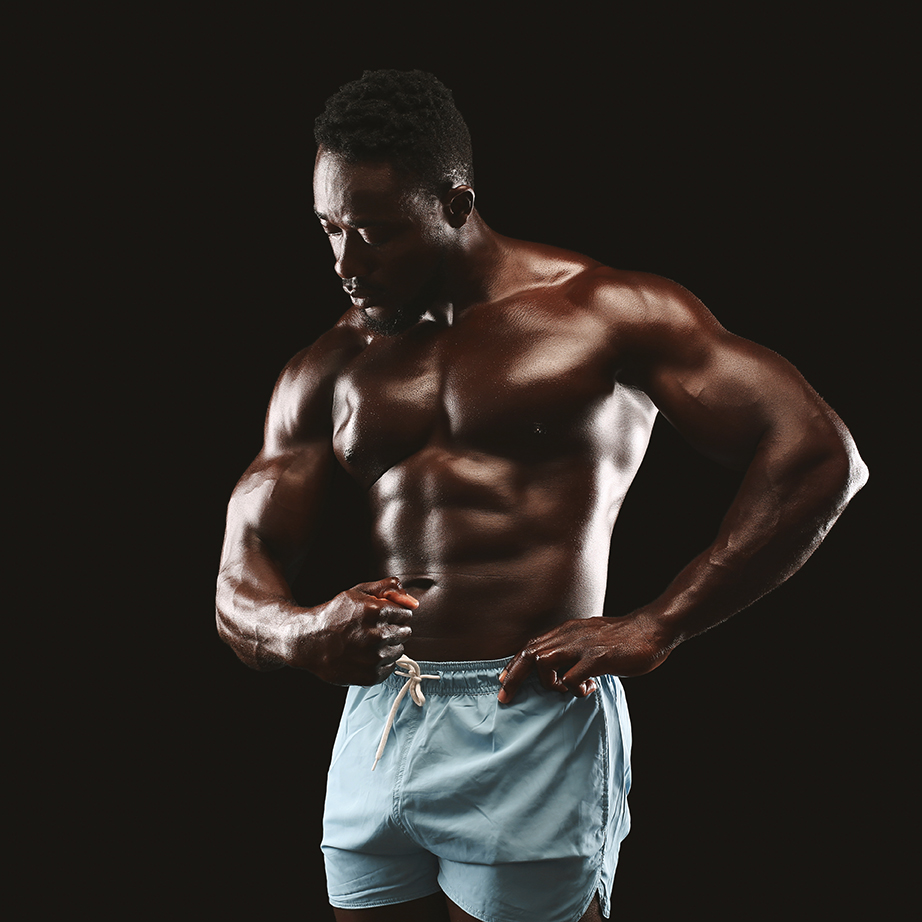 Side Relaxed Pose. Young african american fittness model displaying his abdominals over black background